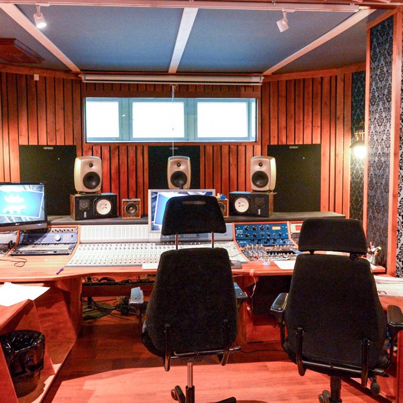 A recording studio - a swivel chair is placed behind an enormous sound board, with a sofa placed at the back of the room